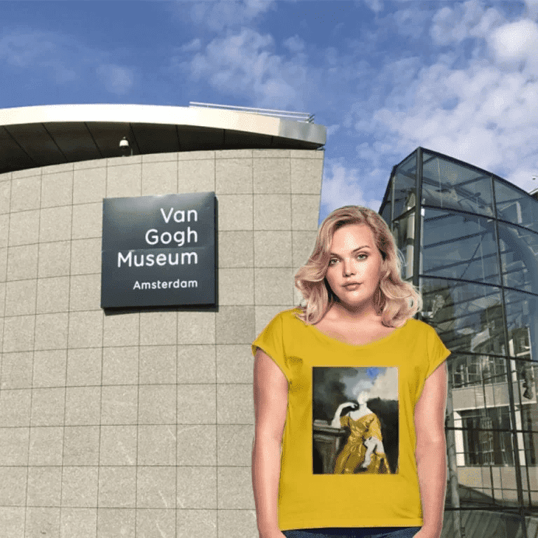 Una mujer con cabello rubio ondulado posa frente al Museo Van Gogh en Ámsterdam. Viste una camiseta de color amarillo vibrante que presenta en el centro una reproducción artística de una mujer con un vestido dorado en una pose clásica. El cielo de fondo está parcialmente nublado y se aprecia la arquitectura moderna del museo.